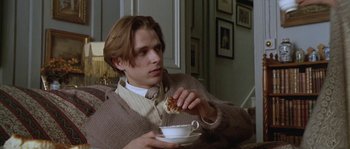 Movie still from “Howards End” (1992), directed by James Ivory – A young man eating a piece of cake while sitting on a couch; Medium shot, Over the shoulder angle