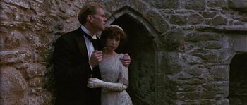 Movie still from “Howards End” (1992), directed by James Ivory – A man and a woman standing next to each other in front of a stone wall; Medium shot, Low angle