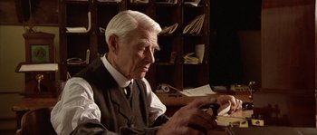 Movie still from “Howards End” (1992), directed by James Ivory – An older man sitting at a desk looking at a book; Close Up shot, Over the shoulder angle