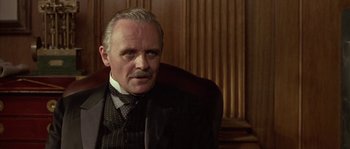 Movie still from “Howards End” (1992), directed by James Ivory – A person sitting in a chair wearing a suit; Close Up shot, Low angle