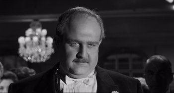 Movie still from “Hush...Hush, Sweet Charlotte” (1964), directed by Robert Aldrich – An older man wearing a suit and bow tie in front of chandeliers; Close Up shot, Over the shoulder angle