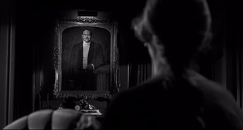 Movie still from “Hush...Hush, Sweet Charlotte” (1964), directed by Robert Aldrich – A black and white photo of a man in a suit and tie in front of a portrait; Medium shot, Over the shoulder angle