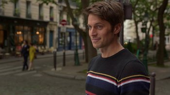 Movie still from “Emily in Paris” (2020), created by Darren Star – A man standing on the sidewalk of a city street; Close Up shot, Over the shoulder angle