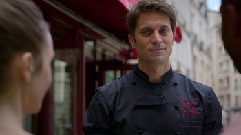 Movie still from “Emily in Paris” (2020), created by Darren Star – A man in a chef's outfit standing in front of a building; Close Up shot, Over the shoulder angle