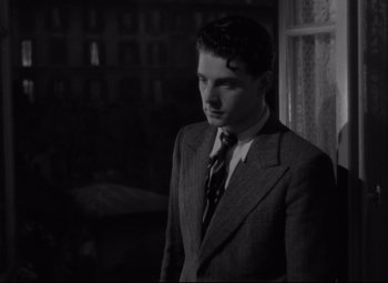 Movie still from “Hotel du Nord” (1938), directed by Marcel Carné – A man wearing a suit and tie standing in front of a window; Medium shot, Low angle