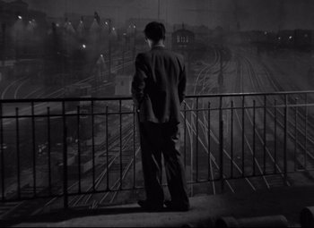 Movie still from “Hotel du Nord” (1938), directed by Marcel Carné – A man standing on a balcony looking out at a train yard; Wide shot, High angle