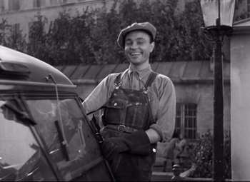 Movie still from “Hotel du Nord” (1938), directed by Marcel Carné – A man in overalls standing next to a car; Medium shot, Low angle