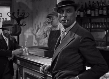 Movie still from “Hotel du Nord” (1938), directed by Marcel Carné – A man smoking a cigarette in a suit and hat; Medium shot, Low angle