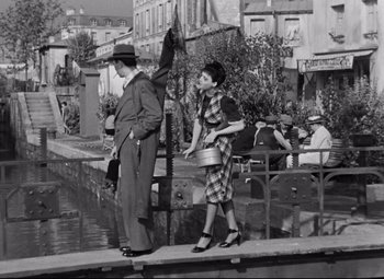 Movie still from “Hotel du Nord” (1938), directed by Marcel Carné – A man and a woman walking on a bridge over a river; Wide shot, High angle
