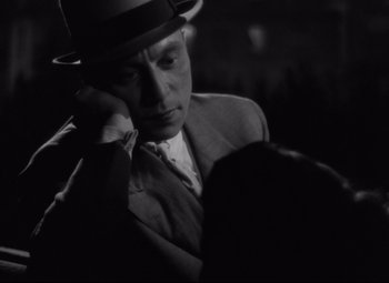Movie still from “Hotel du Nord” (1938), directed by Marcel Carné – A black and white photo of a man in a suit and a hat; Close Up shot, Over the shoulder angle