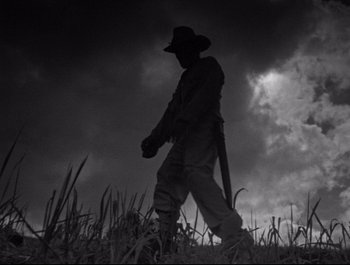 A man walking through a grassy field under a cloudy sky