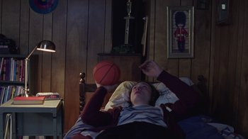 Movie still from “I Am Not a Serial Killer” (2016), directed by Billy O'Brien – A young boy laying in a bed with a basketball; Medium shot, Low angle