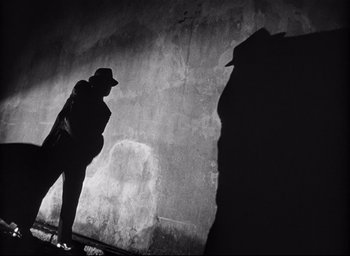 Movie still from “I Confess” (1953), directed by Alfred Hitchcock – A man standing in front of a stone wall; Wide shot, Low angle