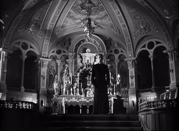 Movie still from “I Confess” (1953), directed by Alfred Hitchcock – A man standing in front of an altar in a church; Wide shot, Low angle
