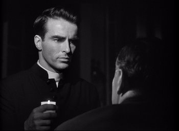 Movie still from “I Confess” (1953), directed by Alfred Hitchcock – A man holding a candle in front of another man; Close Up shot, Over the shoulder angle