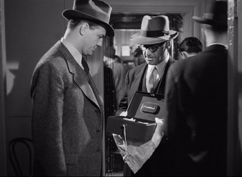 Movie still from “I Confess” (1953), directed by Alfred Hitchcock – A man in a suit and a man in a hat looking at another man in a suit and a hat; Medium shot, Over the shoulder angle