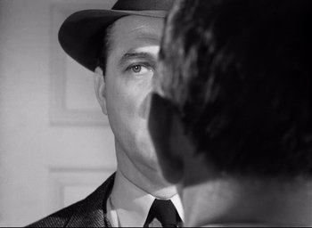 Movie still from “I Confess” (1953), directed by Alfred Hitchcock – A black and white photo of a man wearing a hat; Close Up shot, Over the shoulder angle