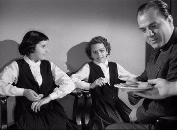 Movie still from “I Confess” (1953), directed by Alfred Hitchcock – A couple of people sitting next to each other in a room; Medium shot, Low angle
