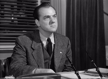 Movie still from “I Confess” (1953), directed by Alfred Hitchcock – A man sitting at a table in front of microphones; Medium shot, Low angle