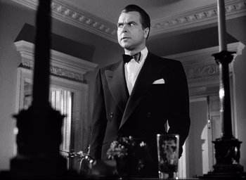 Movie still from “I Confess” (1953), directed by Alfred Hitchcock – A man in a suit and bow tie standing in front of a mirror; Medium shot, Low angle