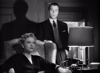 Movie still from “I Confess” (1953), directed by Alfred Hitchcock – A man and a woman sitting in a living room next to each other; Medium shot, Low angle