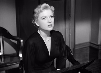 Movie still from “I Confess” (1953), directed by Alfred Hitchcock – A woman sitting in a chair in front of a piano; Close Up shot, Low angle