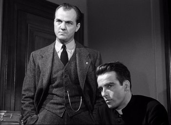 Movie still from “I Confess” (1953), directed by Alfred Hitchcock – Two men are posing for a picture in suits; Medium shot, Low angle