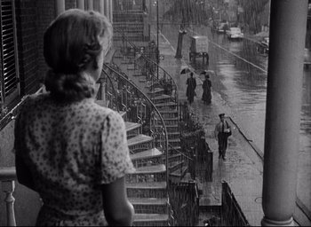 Movie still from “I Confess” (1953), directed by Alfred Hitchcock – An old photo of a woman walking down the stairs in the rain; Wide shot, Low angle