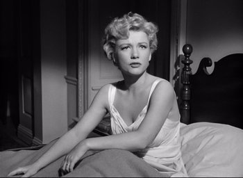 Movie still from “I Confess” (1953), directed by Alfred Hitchcock – A black and white photo of a woman sitting on a bed; Medium shot, Low angle