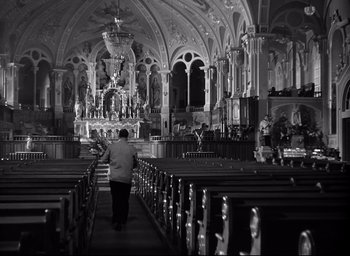 Movie still from “I Confess” (1953), directed by Alfred Hitchcock – A person walking down a church aisle with pews; Wide shot, Low angle
