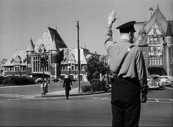 Movie still from “I Confess” (1953), directed by Alfred Hitchcock – An old black and white photo of a man in uniform waving; Wide shot, Low angle