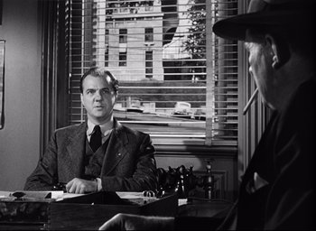 Movie still from “I Confess” (1953), directed by Alfred Hitchcock – A man sitting at a table in front of another man; Medium shot, Over the shoulder angle