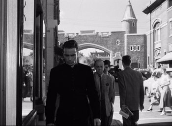 Movie still from “I Confess” (1953), directed by Alfred Hitchcock – A black and white photo of a man walking down the street; Medium shot, Low angle