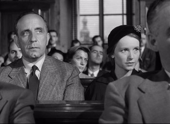 Movie still from “I Confess” (1953), directed by Alfred Hitchcock – A black and white photo of a man and a woman in a courtroom; Medium shot, Low angle