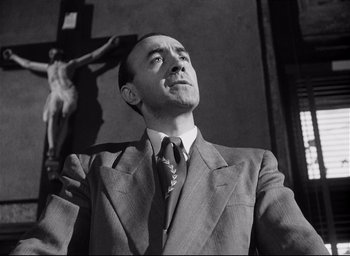 Movie still from “I Confess” (1953), directed by Alfred Hitchcock – A black and white photo of a man in a suit and tie; Close Up shot, Low angle