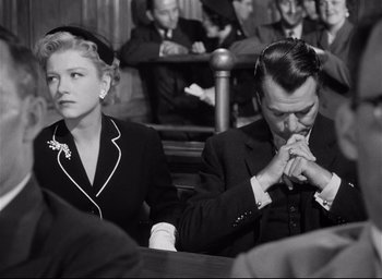 Movie still from “I Confess” (1953), directed by Alfred Hitchcock – A man and a woman sitting next to each other in a courtroom; Medium shot, High angle