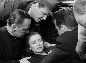 Movie still from “I Confess” (1953), directed by Alfred Hitchcock – A group of men standing around a woman; Medium shot, High angle