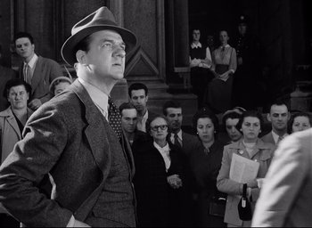 Movie still from “I Confess” (1953), directed by Alfred Hitchcock – An old photo of a man in front of a crowd; Medium shot, Low angle