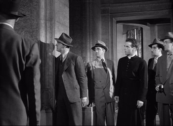 Movie still from “I Confess” (1953), directed by Alfred Hitchcock – A black and white photo of a group of men in suits; Medium shot, Low angle
