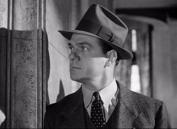 Movie still from “I Confess” (1953), directed by Alfred Hitchcock – A black and white photo of a man wearing a suit and hat; Close Up shot, Low angle