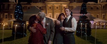 Movie still from “I Give It a Year” (2013), directed by Dan Mazer – A group of people standing next to each other in front of a building; Medium shot, Over the shoulder angle