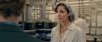Movie still from “I Give It a Year” (2013), directed by Dan Mazer – A woman wearing a head covering in a factory; Close Up shot, Over the shoulder angle