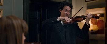 Movie still from “I Give It a Year” (2013), directed by Dan Mazer – A man in a suit and tie playing a violin; Close Up shot, Over the shoulder angle