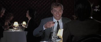 Movie still from “I Heart Huckabees” (2004), directed by David O. Russell – A man sitting at a dinner table holding a wine glass; Medium shot, Over the shoulder angle