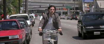 Movie still from “I Heart Huckabees” (2004), directed by David O. Russell – A man riding a bike down a street; Wide shot, Low angle