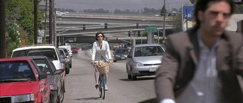 Movie still from “I Heart Huckabees” (2004), directed by David O. Russell – A woman riding a bike down a street with traffic; Wide shot, Over the shoulder angle
