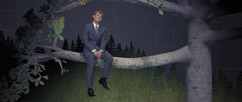 Movie still from “I Heart Huckabees” (2004), directed by David O. Russell – A man in a suit and tie sitting on a tree branch; Wide shot, Low angle