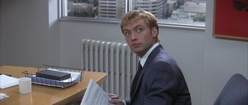 Movie still from “I Heart Huckabees” (2004), directed by David O. Russell – A man sitting at a desk in front of a window holding papers; Close Up shot, Over the shoulder angle