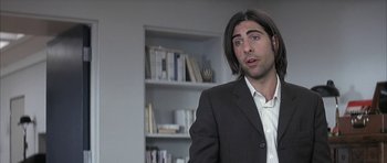 Movie still from “I Heart Huckabees” (2004), directed by David O. Russell – A man with long hair and a suit is standing in front of a book shelf; Close Up shot, Over the shoulder angle
