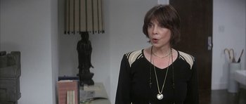 Movie still from “I Heart Huckabees” (2004), directed by David O. Russell – A woman in a black and white outfit standing next to a table; Close Up shot, Over the shoulder angle
